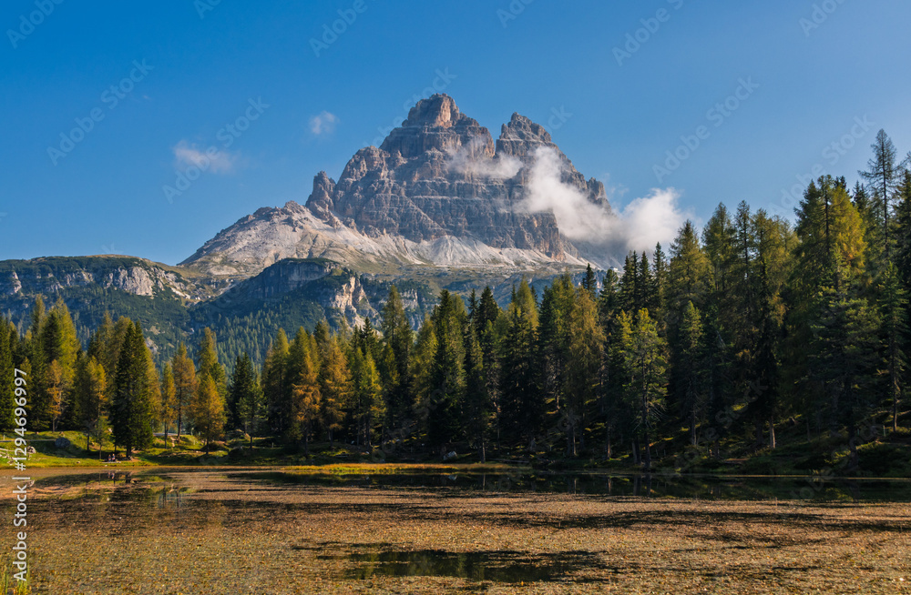 Tre Cime di Lavaredo during sunrise with warm golden light and a lake in the foreground