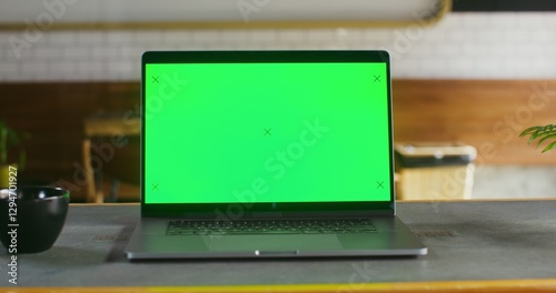 Fotografie open laptop with a green screen stands on a table in coffee shop open laptop with a green screen stands on a table in a coffee shop, close-up