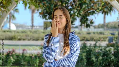 A young businesswoman in a tree-filled park on a spring day, looking at the camera with facial expressions that indicate she is feeling nauseous