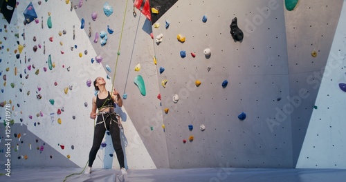 A young woman pulls on a safety rope for a man descending from a climbing wall while standing at the foot of the wall. limbing workout on an artificial surface in the indoor gym