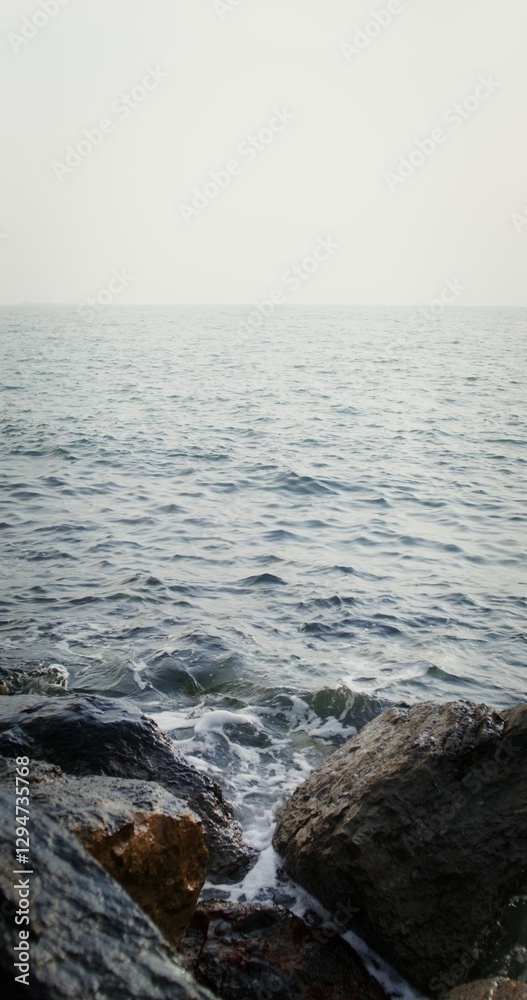 Fototapeta premium Sea waves hit large rocks on the coast, foaming and splashing as they wash over the boulders. Vertical video on a sunny day. 4k video, red komodo