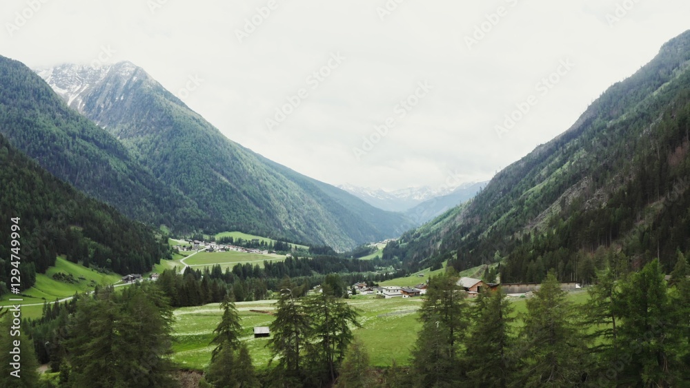 Obraz premium Beautiful panormany view of the high mountain valley with the village in the lowland. The peaks of the rocky Alpine mountains are covered with snow. Austria