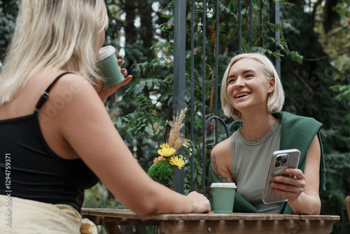 Obraz na płótnie Two friends are enjoying a cheerful conversation over coffee at an outdoor table surrounded by nature