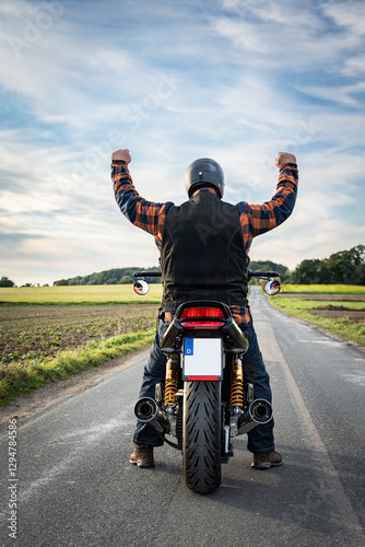 Fotografia Motorradfahrer auf seiner Maschine von hinten in Siegerpose, Rückansicht