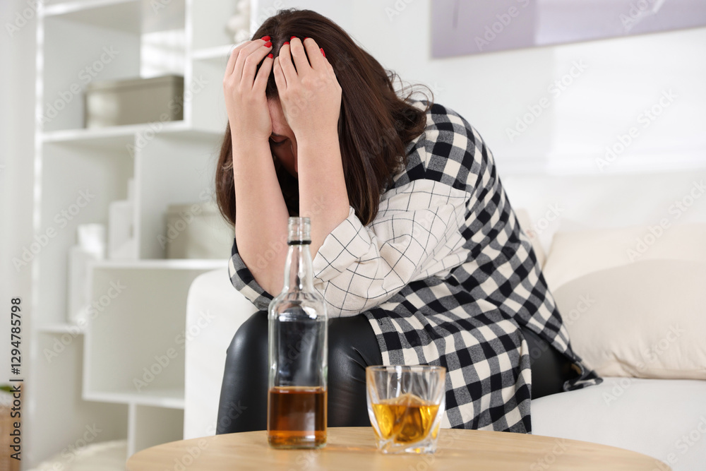 Alcohol addiction. Woman near wooden table with glass of whiskey and bottle at home Alcohol addiction. Woman near wooden table with glass of whiskey and bottle at home