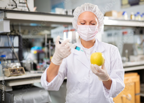 Professional female geneticist working in laboratory, injecting additives into apple during experiments with genetically modified apple