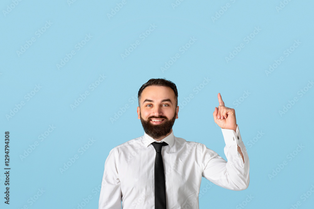 Happy millennial businessman in formalwear pointing upwards at empty space on blue studio background. Attractive bearded CEO having creative idea, gesturing eureka, experiencing aha moment