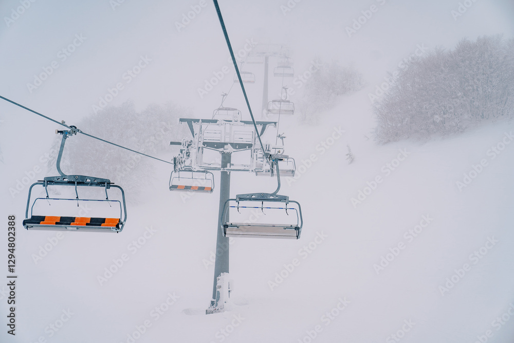 Quadruple chairlift rises above snowy forest to misty mountain Quadruple chairlift rises above snowy forest to misty mountain