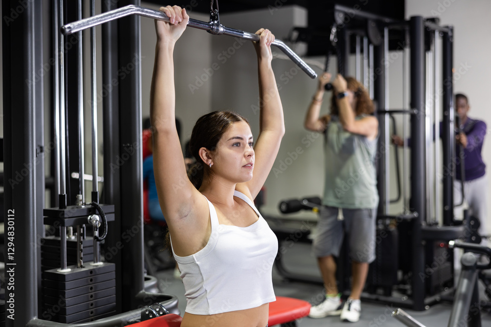 Fototapeta premium Caucasian woman training on lat pull down machine in gym