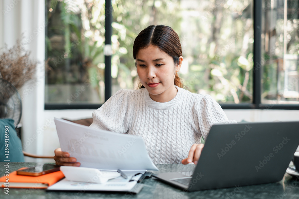 A focused young woman working from home, reviewing documents with a laptop in a bright, modern workspace. A focused young woman working from home, reviewing documents with a laptop in a bright, modern workspace.