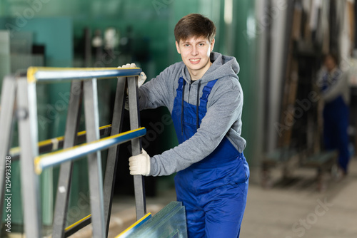 Guy glazer employee in blue overall works in glass processing shop. He carries out installation work, products for renovation of residential premises made of glass and plastic..