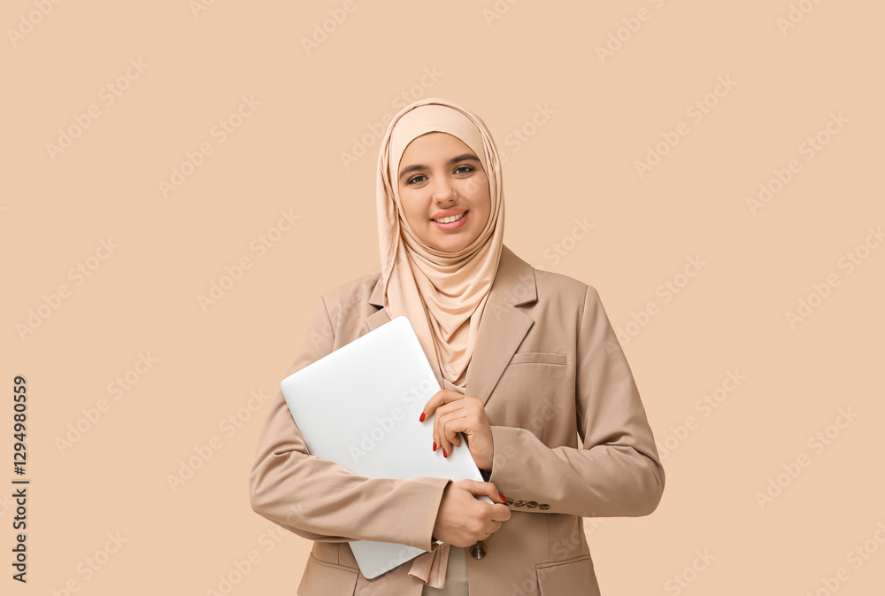 Fototapeta premium Beautiful young Muslim woman in hijab with modern laptop on beige background