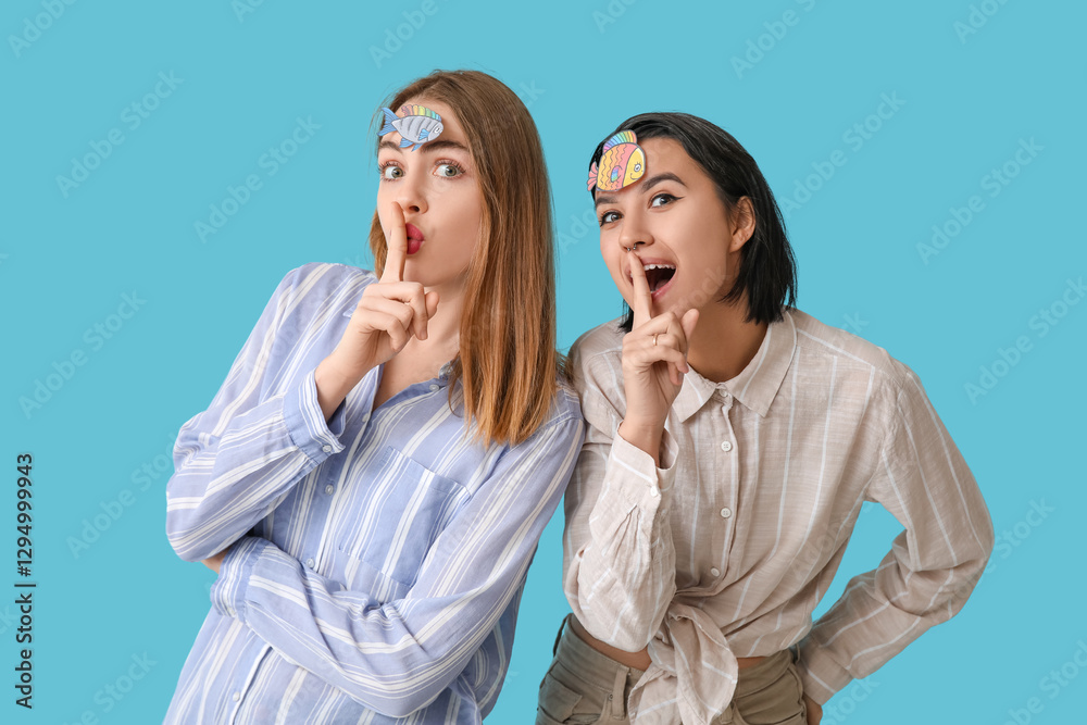 Φωτογραφία Beautiful young women with paper fishes attached to their foreheads showing silent gesture on blue background