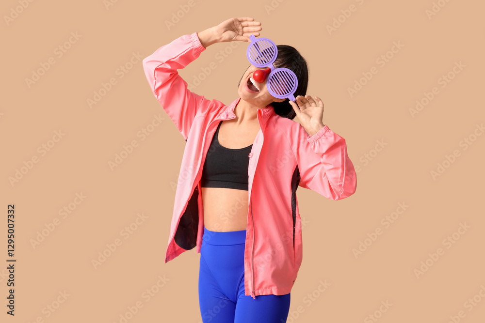 Obraz premium Young smiling female fitness trainer with funny glasses on beige background. Fool's day