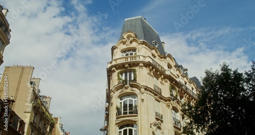 The facade of triangular historical building with a corner at crossroads and widening edges of the walls. Windows and balconies are covered with green vegetation. Paris, France. 4k video, red komodo