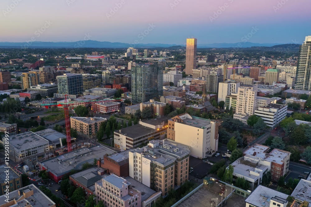 High-angle view of Portland, Oregon's downtown skyline at twilight. Modern and historic buildings, construction crane, and city streets are visible. Oregon, USA High-angle view of Portland, Oregon's downtown skyline at twilight. Modern and historic buildings, construction crane, and city streets are visible. Oregon, USA