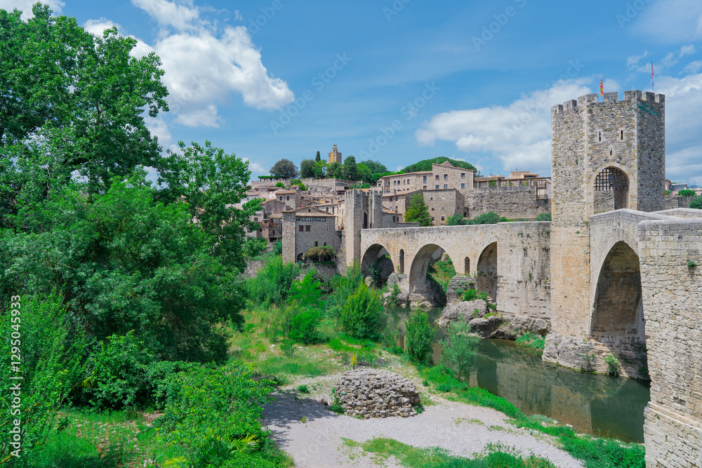 Puente medieval sobre un rio con vegetación, un dia soleado con cielo azul y nubes. Desde Besalú, Gerona, Cataluña, España. Puente medieval sobre un rio con vegetación, un dia soleado con cielo azul y nubes. Desde Besalú, Gerona, Cataluña, España.