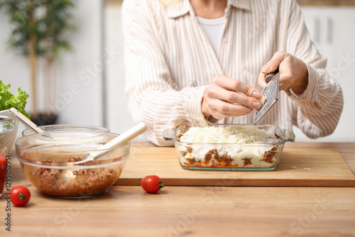 Beautiful mature woman grating cheese for delicious lasagna at table in kitchen, closeup