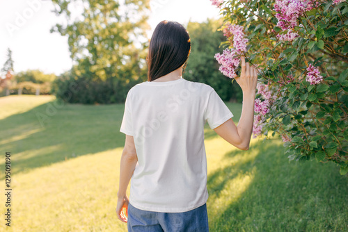 A young woman wearing a white plain T-shirt outdoors, green nature background. Mockup for design, template. Back view