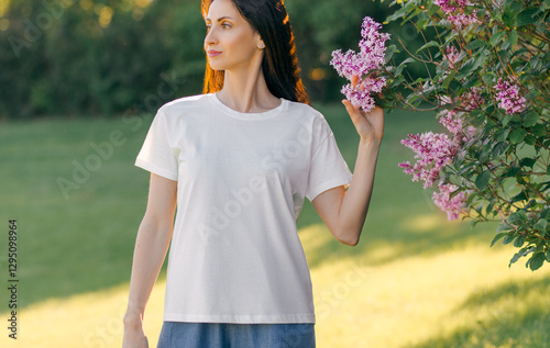 A young woman wearing a white plain T-shirt outdoors, green nature background. Mockup for design, template. Front view