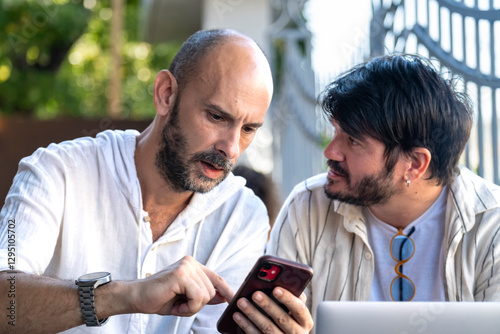 Two middle-aged men professionals happily work on their laptops in the garden of a cafe on a summer day