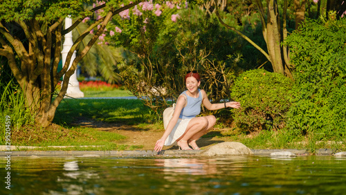 Tablou pe pânză A beautiful red-haired young woman models stylishly by a river in a wooded area