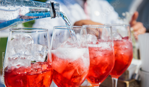 The bartender pours soda into a glass of wine with ice in close-up. Creating a red cocktail, wine, juice, liqueur, bubbling water. Refreshing cocktail in summertime. Beach bar, sun, cold drinks