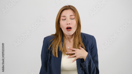 In a studio setting, a young businesswoman wearing a suit is standing in front of a white background, gagging as if feeling nauseous and looking at the camera