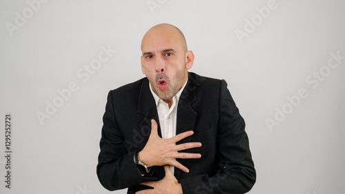In a studio setting, a middle-aged businessman wearing a suit is standing in front of a white background, gagging as if feeling nauseous and looking at the camera