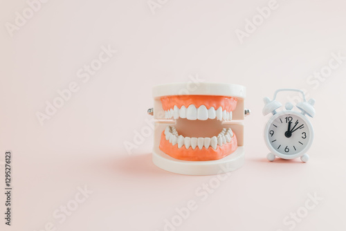 Dentist Day concept. White alarm clock and tooth model on pink background