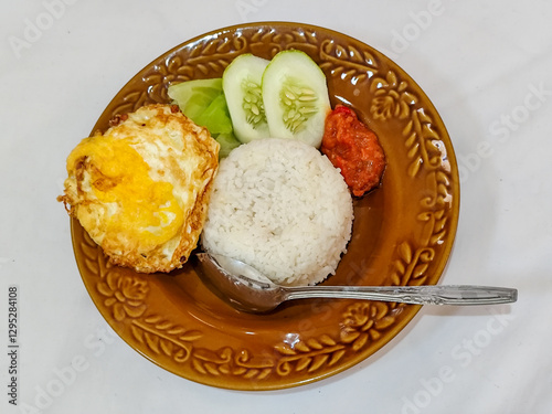 Lalapan Telur.  Rice with fresh vegetables, with traditional Indonesian chili sauce, with fried egg side dish, white background.