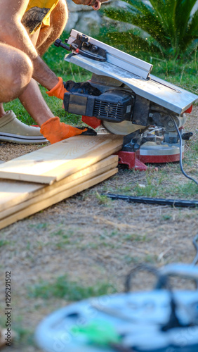 A middle-aged man cutting timber with a circular saw in the garden of his house on a summer day