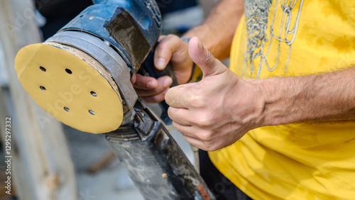 A middle-aged man sanding timber with a sander in the garden of his house on a summer day