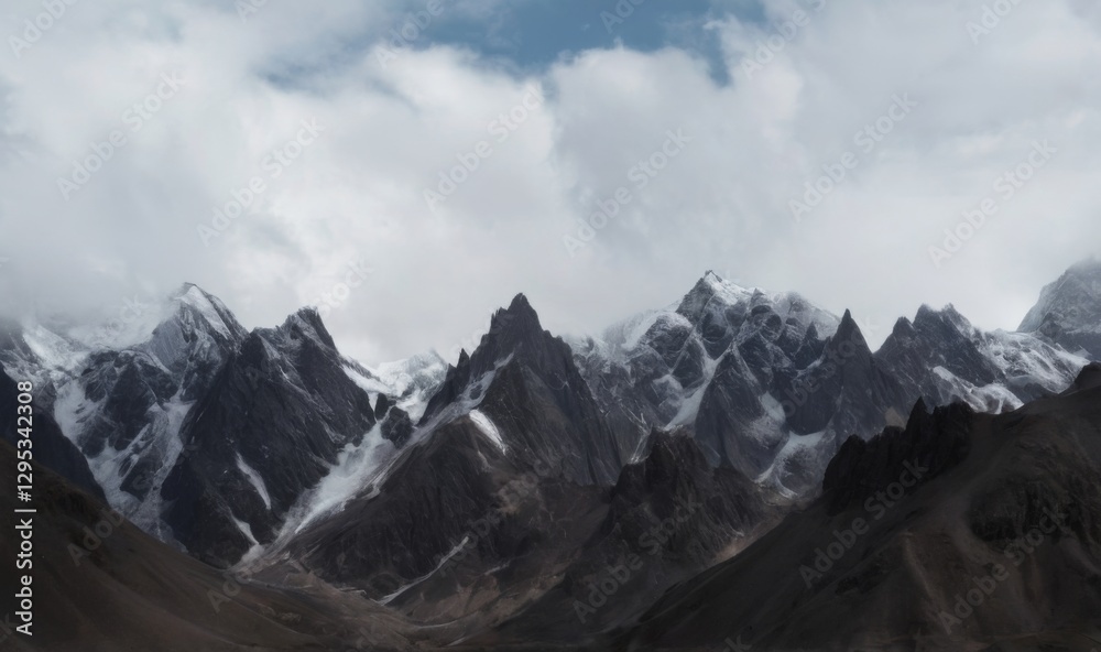 Obraz premium Snowcovered mountain range under fluffy clouds showing dramatic, aweinspiring landscape with jagged peaks and deep valleys.