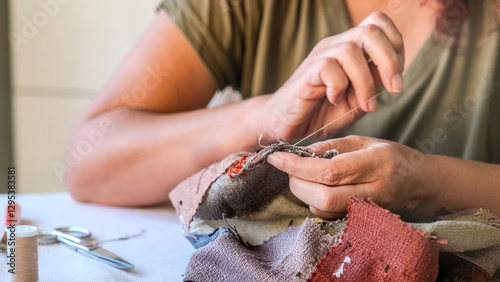 A close-up image of the hands of a middle-aged woman sewing a bag with needle and thread while sitting at home