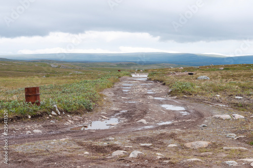 Rocky road through the tundra, large stones, puddles after rain, cloudy sky. Rybachy Peninsula, Murmansk region, Russia photo