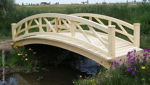 A wooden arched bridge spans a small stream surrounded by green grass