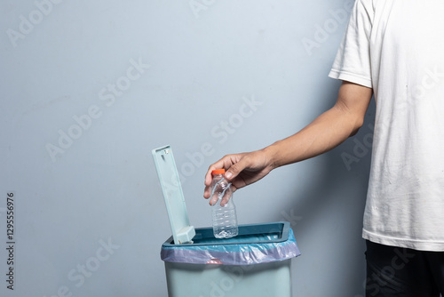 A man's hand is about to throw a water bottle into the trash.