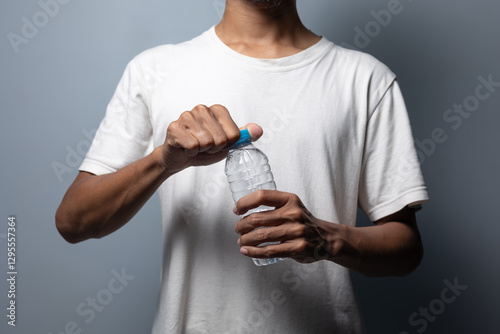 A man wearing a white t-shirt holds a water bottle and tries to open it.