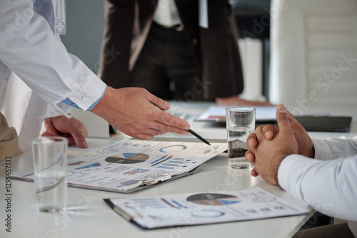 Side view closeup of unrecognizable doctors discussing medical data and pointing at clipboard with statistics reports during meeting copy space