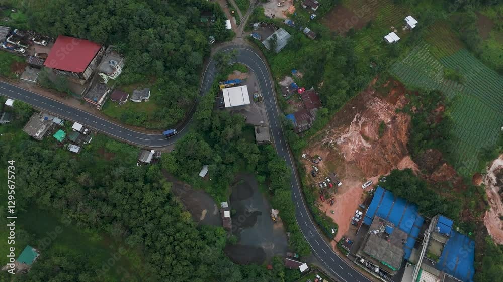 A high drone shot captures Meghalaya’s winding roads, as vehicles navigate the smooth curves, surrounded by lush green landscapes.