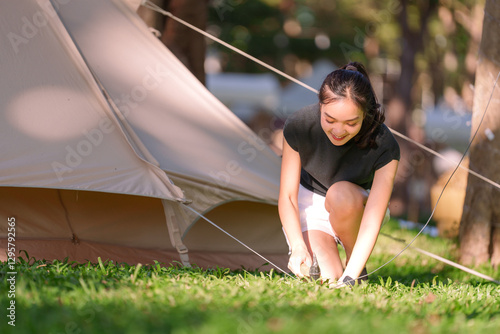 Fotografie Young asian woman hammering tent stakes into the ground while setting up a tent