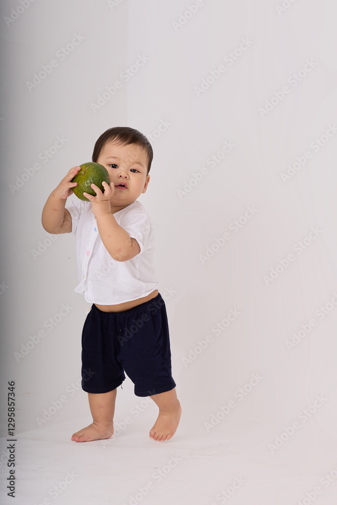 .The baby is holding a green fruit in his hand and appears to be enjoying it. The image captures the baby's playful moment as he holds up the fruit.