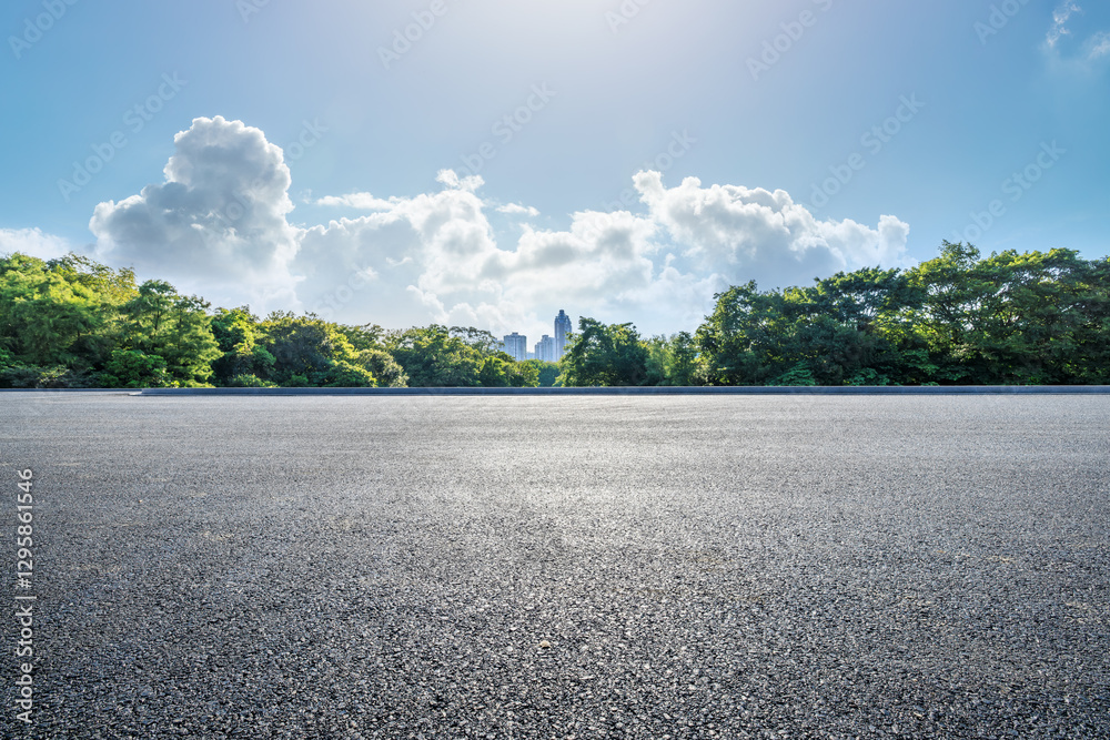Empty asphalt road with green trees and city buildings in the distance under blue sky