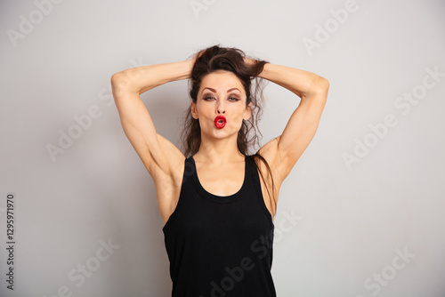 Happy beautiful make-up woman with red lipstick looking in black summer top brash showing the lips kiss sign on white empty studio wall copy space background. Expression fun portrait.