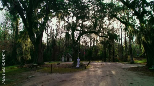 Wallpaper Mural Historic tiny chapel surrounded by majestic oak trees and Spanish moss, featuring a serene dirt path and memorial statue in a tranquil forest setting. Torontodigital.ca