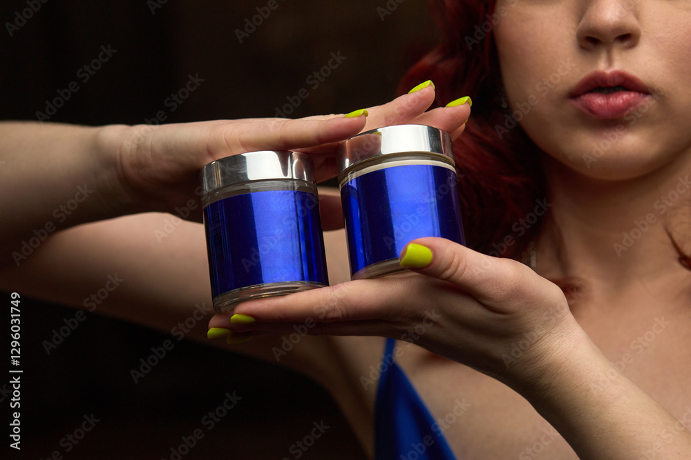 Woman displaying, vibrant blue jars held in hands, close-up with bright manicure, elegant presentation, beauty products concept