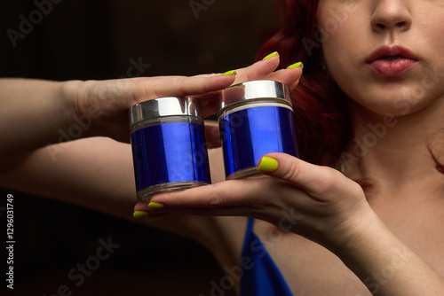 Obraz na płótnie Woman displaying, vibrant blue jars held in hands, close-up with bright manicure, elegant presentation, beauty products concept w salonie