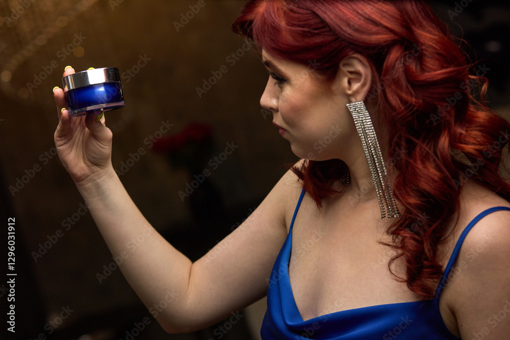 Woman admiring luxurious blue cosmetic jar in elegant setting, beauty care idea, elegant evening concept