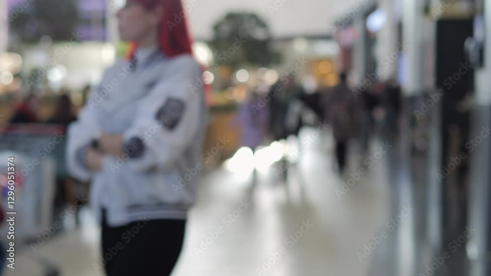 A blurry image of a busy shopping mall with people walking around and sitting at tables. Scene is bustling and lively, with people going about their day